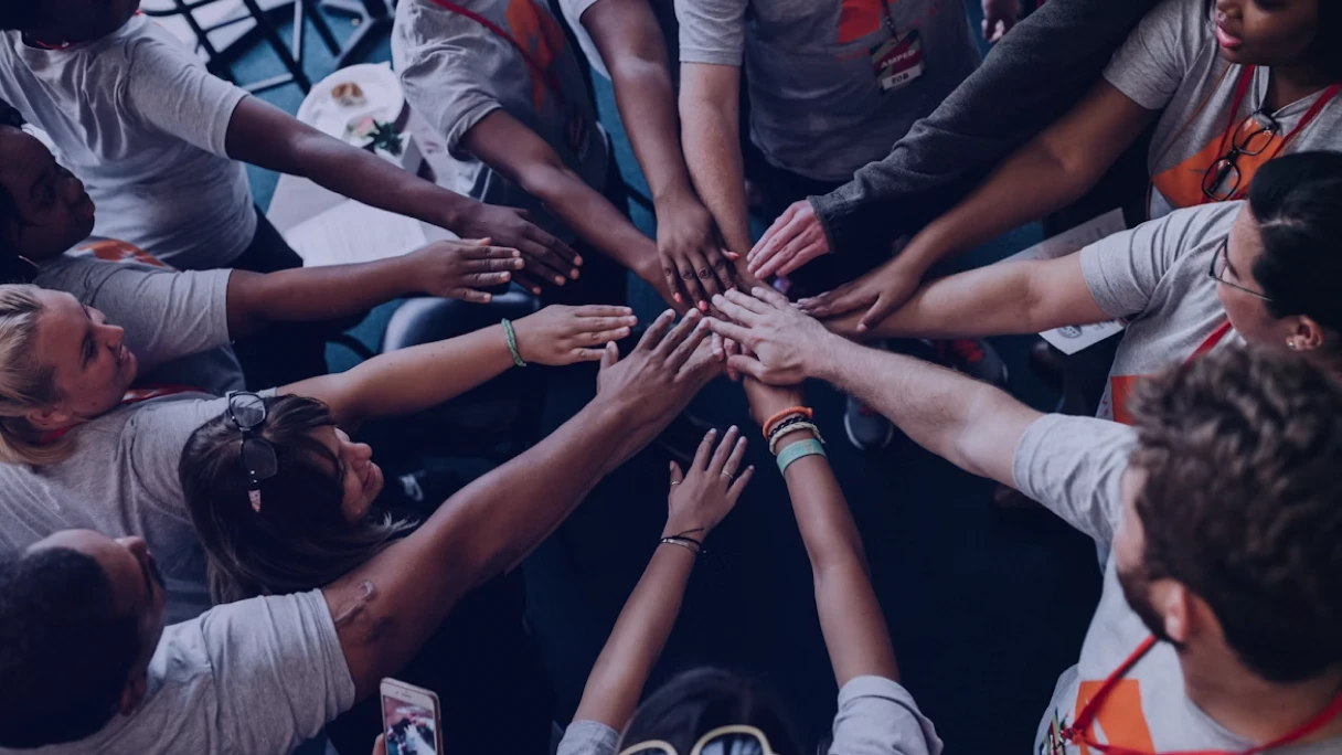 Grupo diverso de voluntários unindo as mãos ao centro, simbolizando o encontro entre voluntariado corporativo e diversidade